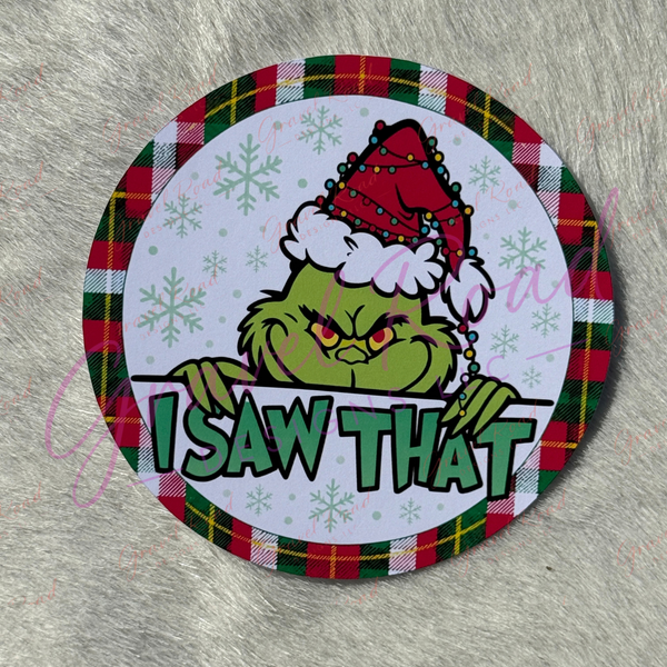 A round cardstock featuring G peeking over a white banner with the text 'I SAW THAT' in green letters. G is wearing a red Santa hat with white trim. pictured on a faux fur backdrop