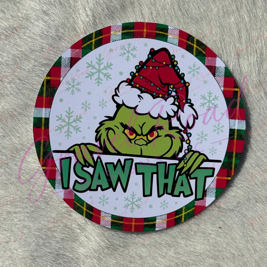 A round cardstock featuring G peeking over a white banner with the text 'I SAW THAT' in green letters. G is wearing a red Santa hat with white trim. pictured on a faux fur backdrop