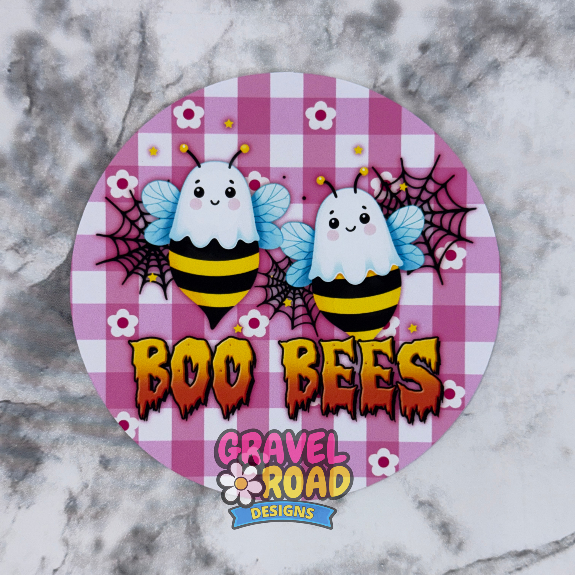 A round cardstock featuring two cute cartoon ghosts and bees on a pink and purple checkered background with the text 'BOO BEES' and the logo 'Gravel Road Designs' at the bottom, displayed on a gray marble surface.