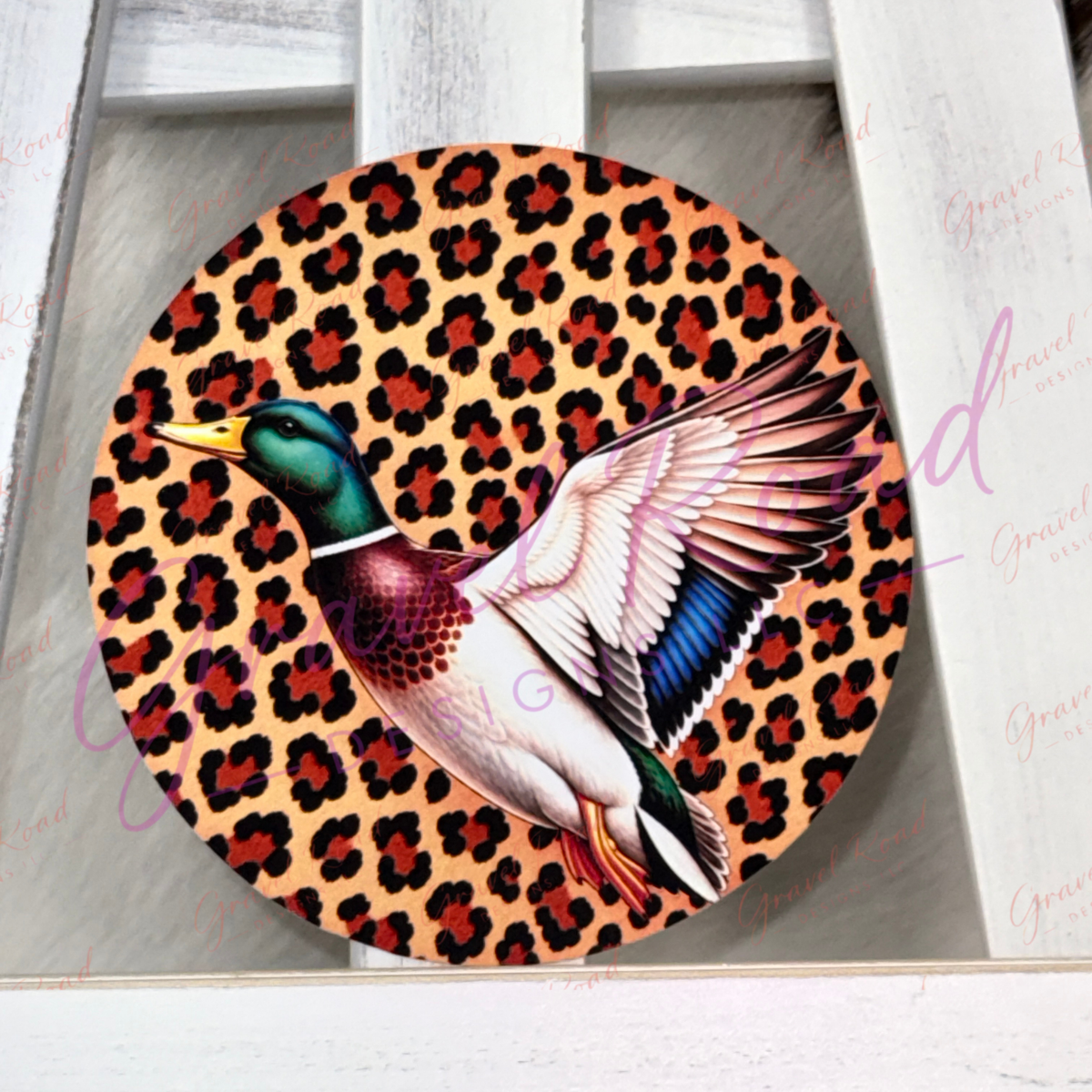 A round cardstock featuring a flying mallard duck over a leopard print background, displayed on a white wooden surface.