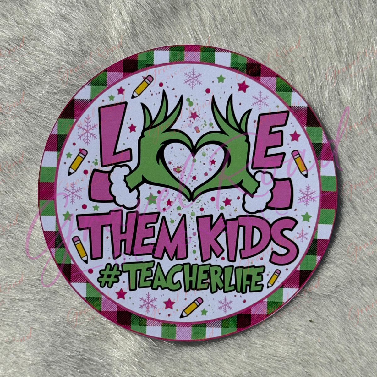 A round printed cardstock with a festive holiday design, featuring the text 'LOVE THEM KIDS #TEACHERLIFE' with a green heart made from hands, set against a gray faux fur background.
