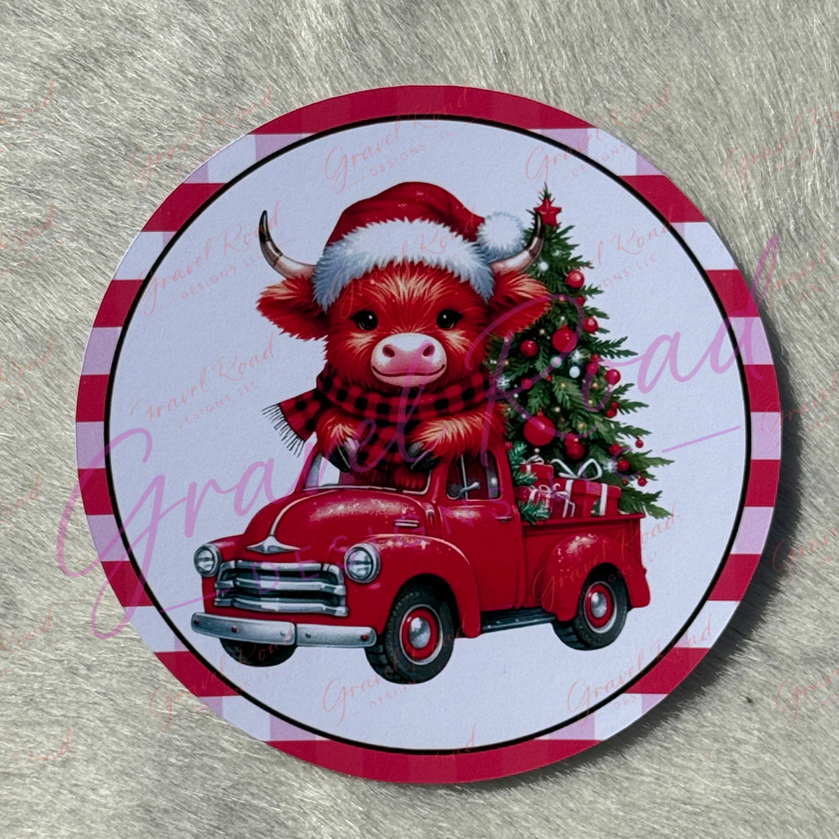 A round printed cardstock featuring a red vintage truck carrying a decorated Christmas tree and a Highland Cow wearing a red-and-black plaid  scarf and a Santa hat, centered on a gray textured background.