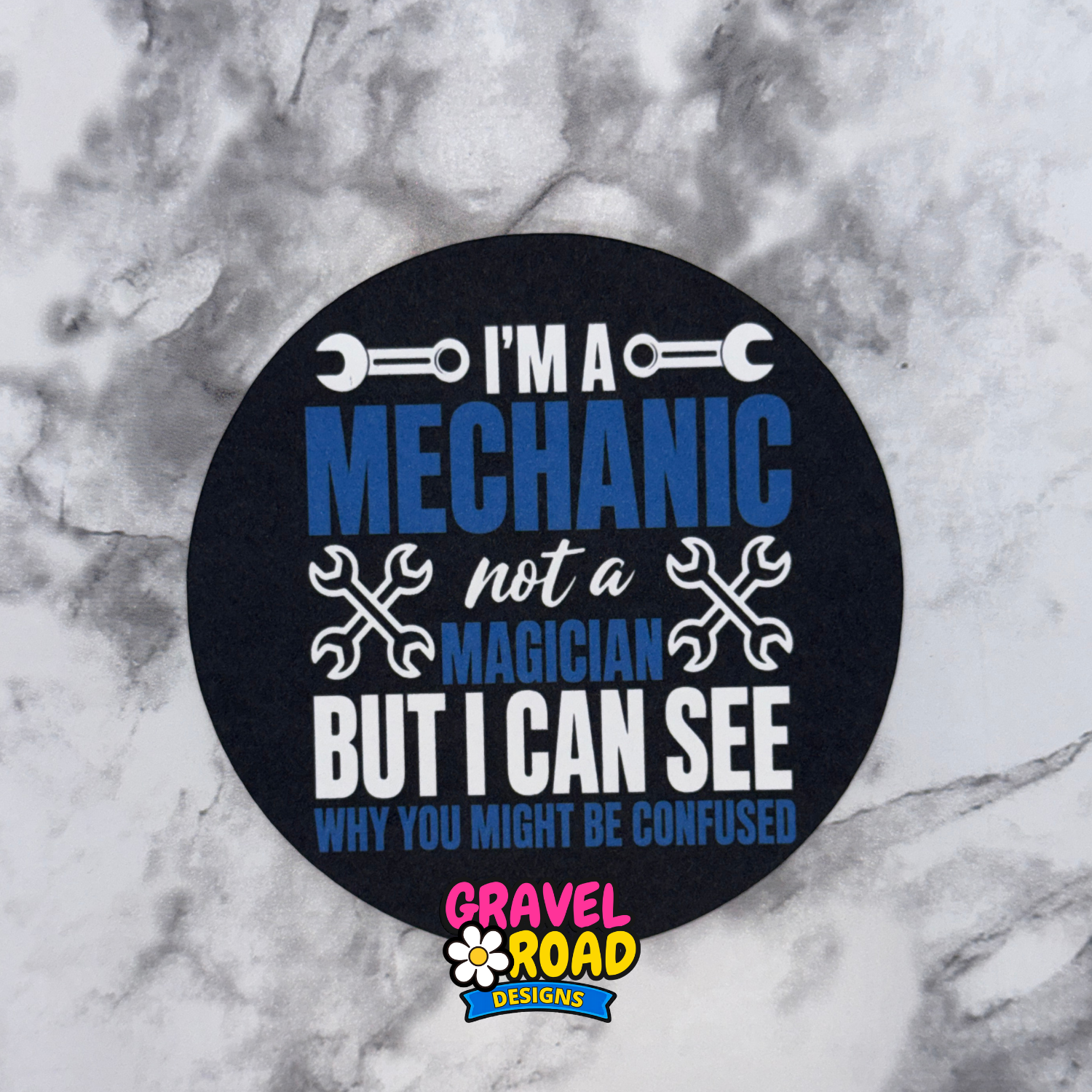 Round black cardstock with text 'I'm a mechanic not a magician but I can see why you might be confused' on a marble background.