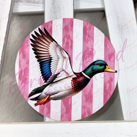 A round cardstock featuring a flying mallard duck over pink and white vertical stripes, displayed on a white wooden surface.