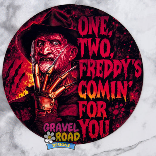 A circular cardstock design featuring Freddy Krueger with the text 'ONE, TWO, FREDDY'S COMIN' FOR YOU' on a white marble background. The Gravel Road Designs logo is visible at the bottom.