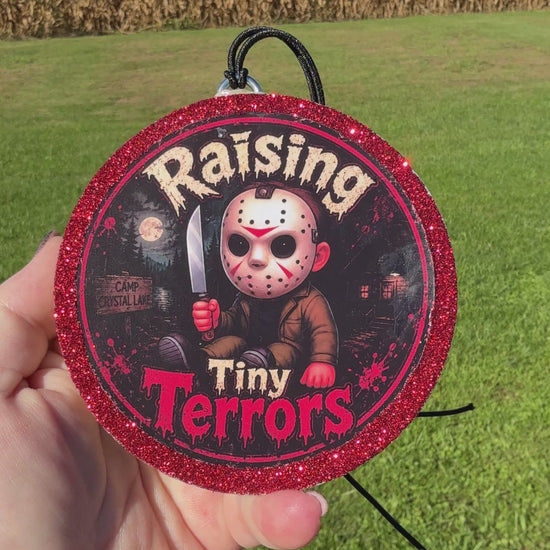 A video showing a Cartoon child horror‑themed freshie with a glittery red border, black hanging cord, and “Raising Tiny Terrors” text in front of a moonlit forest and camp sign