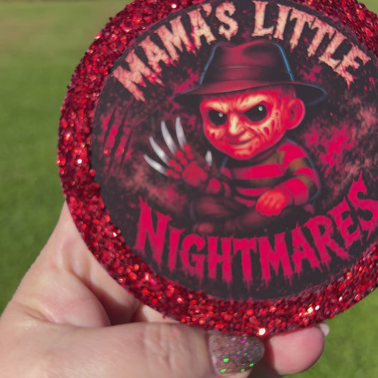 A video showing a Cartoon character‑style horror freshie with a glittery red border, black hanging cord, and “Mama’s Little Nightmares” text on a red splatter background.